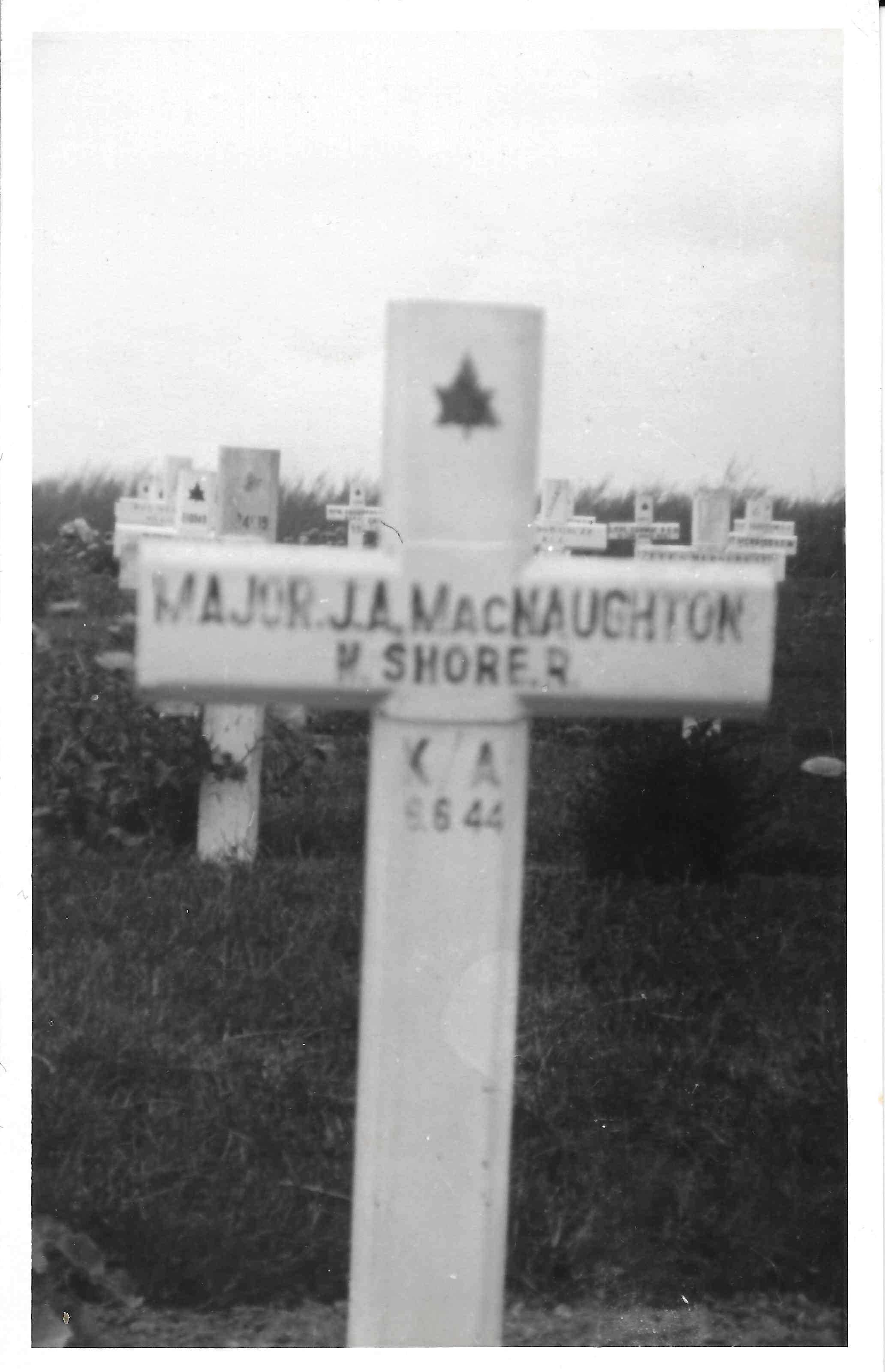 Une image en noir et blanc montre une croix en bois blanche marquant une tombe.